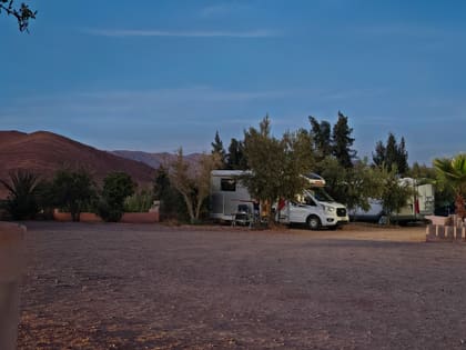 Wohnmobile auf einem Stellplatz bei Taznakhte, dahinter die Berge im Abendlicht