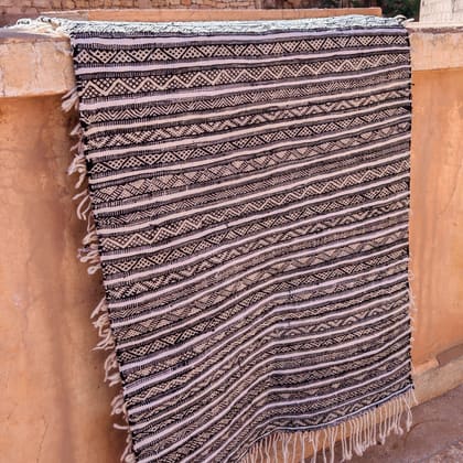 Ein schwarz-weiß gemusterter Teppich hängt über einer Lehmmauer
